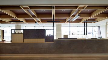 A modern interior with a reception desk, large windows, and a ceiling with exposed beams.
