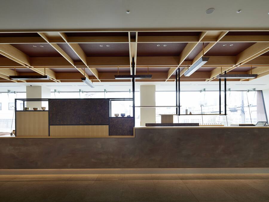 A modern interior with a reception desk, large windows, and a ceiling with exposed beams.
