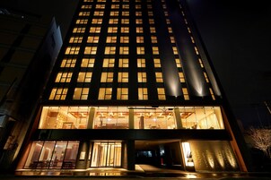 Un edificio de gran altura con ventanas iluminadas y una entrada a nivel de calle con puertas de vidrio.