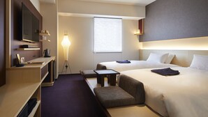 Una habitación de hotel con dos camas, televisor, escritorio y lámpara.