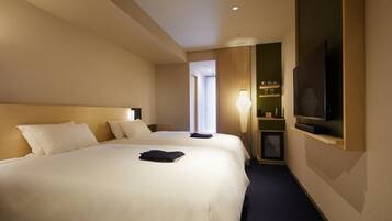 A hotel room with two beds, a TV mounted on the wall, a bedside table, and a lamp.
