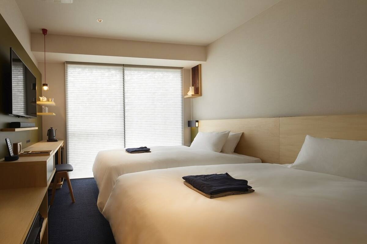 Ein Hotelzimmer mit zwei Betten, einem Schreibtisch, einem Fernseher und einem Fenster mit Jalousien.