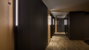 Pasillo moderno de hotel con paredes oscuras, iluminado por tiras verticales de luz y suelo alfombrado.