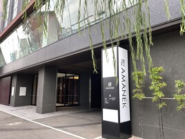 Un edificio moderno con un letrero que dice 'AMANEK HOTEL', indicando la entrada al vestíbulo.