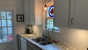 A modern kitchen with white cabinets, a stainless steel sink, a coffee maker, and a window with a stained glass view.