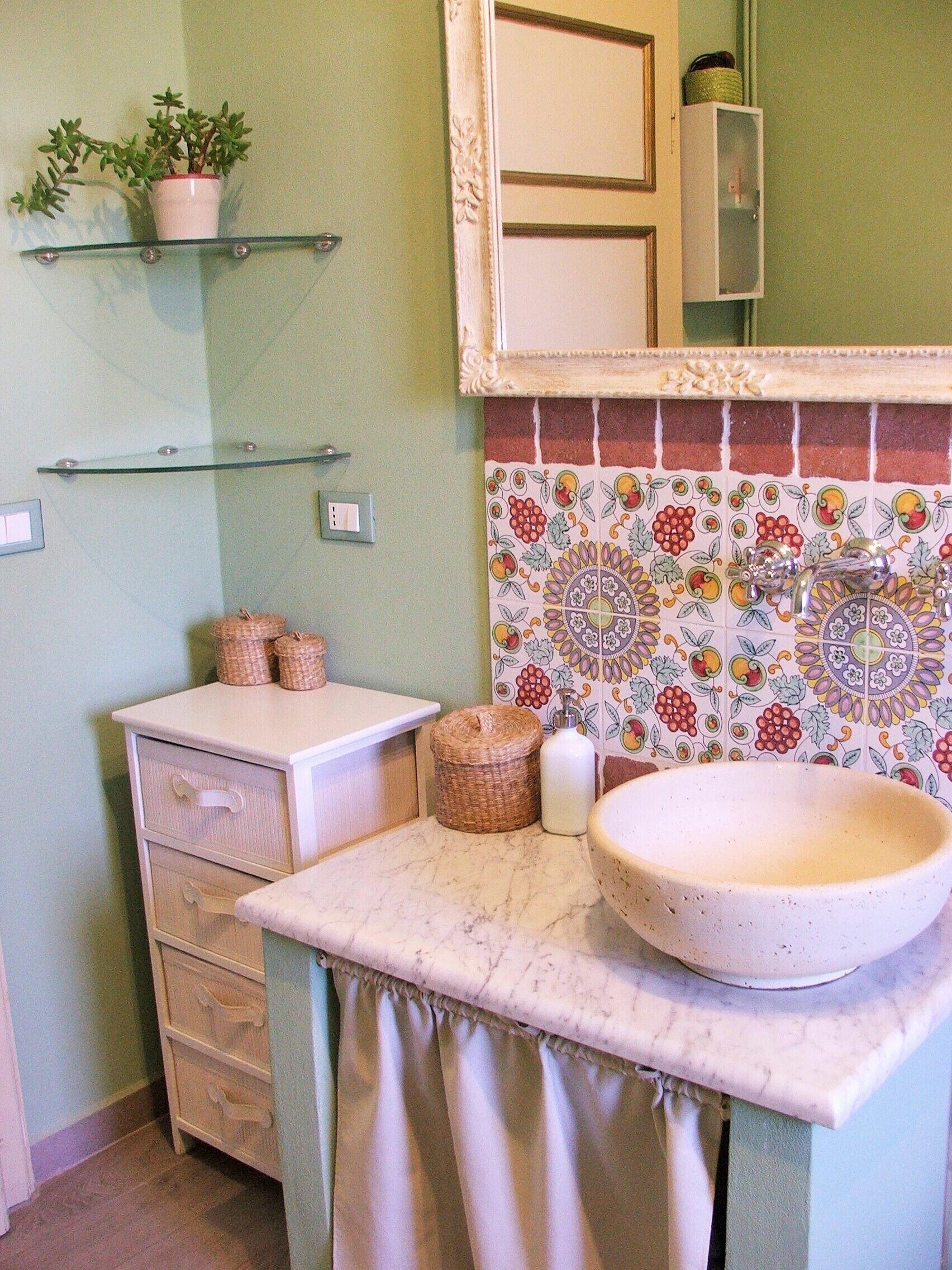 A bathroom with a white sink, a mirror, a potted plant, and a tiled backsplash.