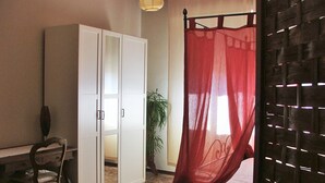 A room with a bed covered by a red canopy, a white wardrobe, a desk with a chair, and a potted plant.
