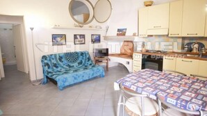 A cozy living area with a sofa, a dining table with chairs, a kitchen area with cabinets, and a ceiling with wooden beams. - Two-room apartment Piazza al Fico 2/4 Beds in the historic center of Portoferraio (PORTOFERRAIO)