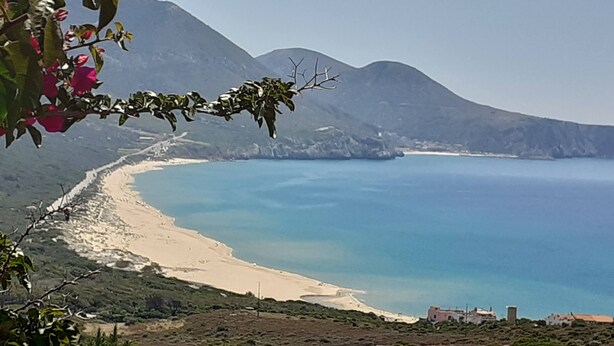Un paysage côtier avec une plage, des montagnes et un ciel dégagé.