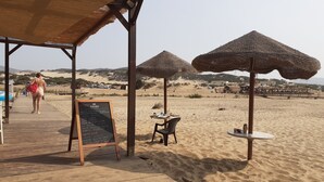 Un café situé en bord de mer, doté d’une terrasse en bois, de parasols en chaume et d’un tableau noir servant de menu.