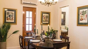 A dining room with a round table set for four, framed botanical prints on the walls, a chandelier, and a potted plant. - 7 BRD  "The Coral Penthouse" w/360° | Beach | AC All Rm (Rio de Janeiro)