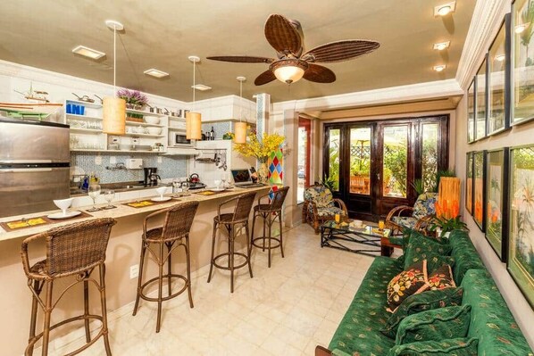 A modern kitchen with a central island, bar stools, and a dining area with a green sofa.