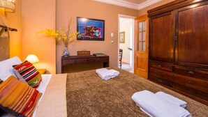 Une chambre d’hôtel avec un lit, une armoire en bois, une table de chevet avec une lampe, un tableau encadré au mur et un vase avec des fleurs.