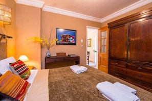 A hotel room with a bed, a wooden wardrobe, a nightstand with a lamp, a framed picture on the wall, and a vase with flowers. - 7 BRD  "The Coral Penthouse" w/360° | Beach | AC All Rm (Rio de Janeiro)