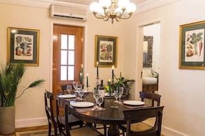 A dining room with a round table set for four, framed botanical prints on the walls, a chandelier, and a potted plant. - 7 BRD  "The Coral Penthouse" w/360° | Beach | AC All Rm (Rio de Janeiro)