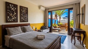 A hotel room with a bed, a desk, a chair, a balcony with plants, and a view of buildings. - 7 BRD  "The Coral Penthouse" w/360° | Beach | AC All Rm (Rio de Janeiro)
