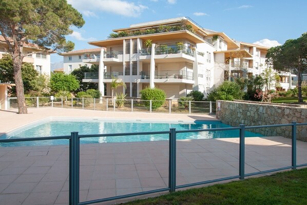 A modern apartment building with a swimming pool, balconies, and a stone wall.