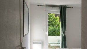 Ein Schlafzimmer mit einem Bett, einer Glasschiebetür zu einem Außenbereich mit Tisch und Stühlen sowie einem Fenster mit Vorhängen.