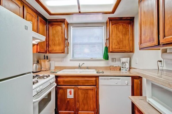 A compact kitchen with wooden cabinets, a white refrigerator, a stove, a sink, and a dishwasher.