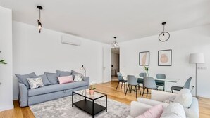 A modern living room with a grey sofa, a coffee table, and a dining area with chairs and a table. - Lovage Gray Apartment, Benfica, Lisbon (Lisboa)