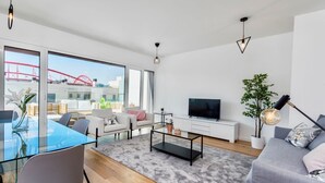 A modern living room with a glass dining table, grey sofa, and a flat-screen TV. - Lovage Gray Apartment, Benfica, Lisbon (Lisboa)