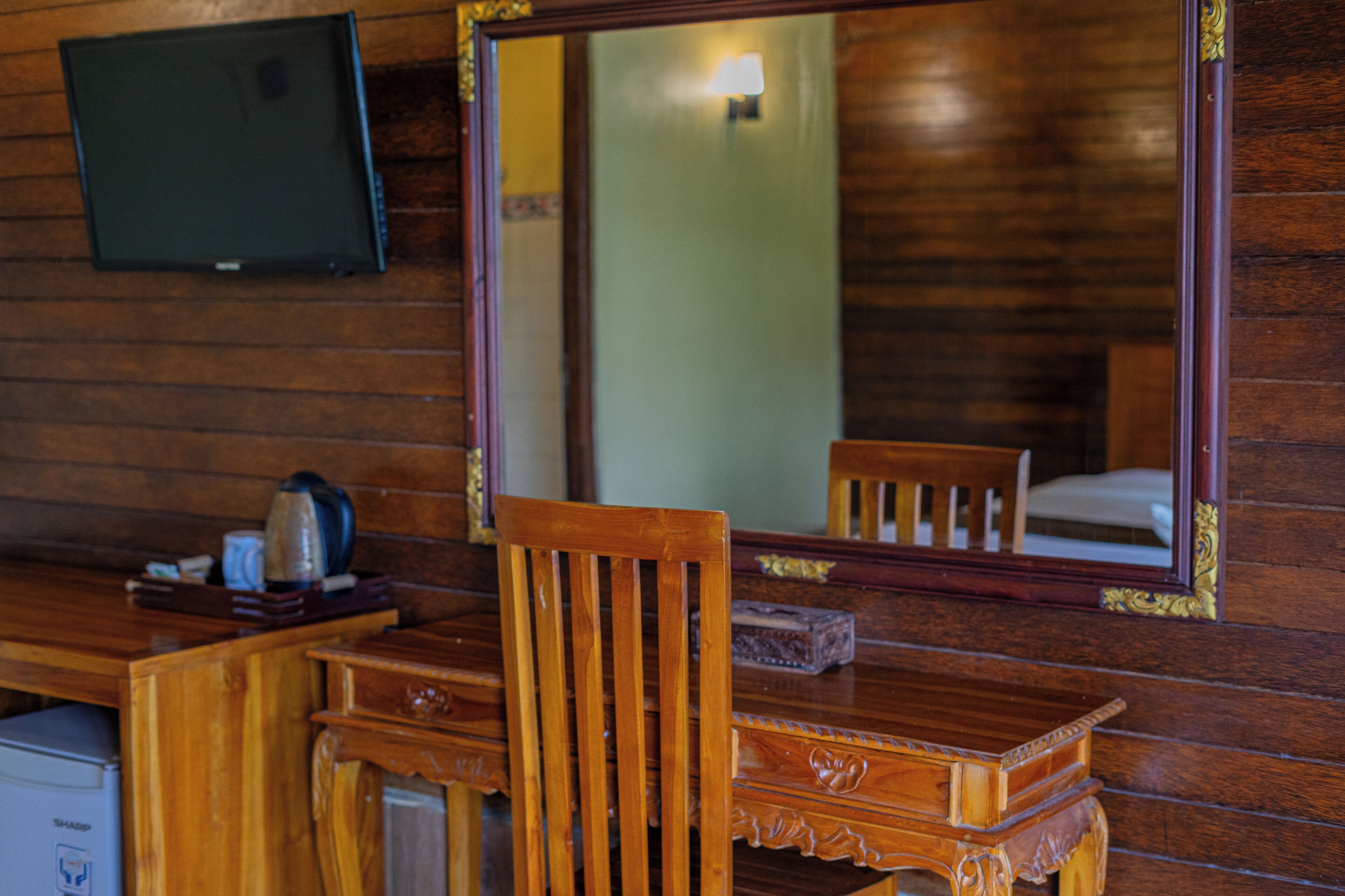 A wooden room with a large mirror, a wooden desk, and a television mounted on the wall.