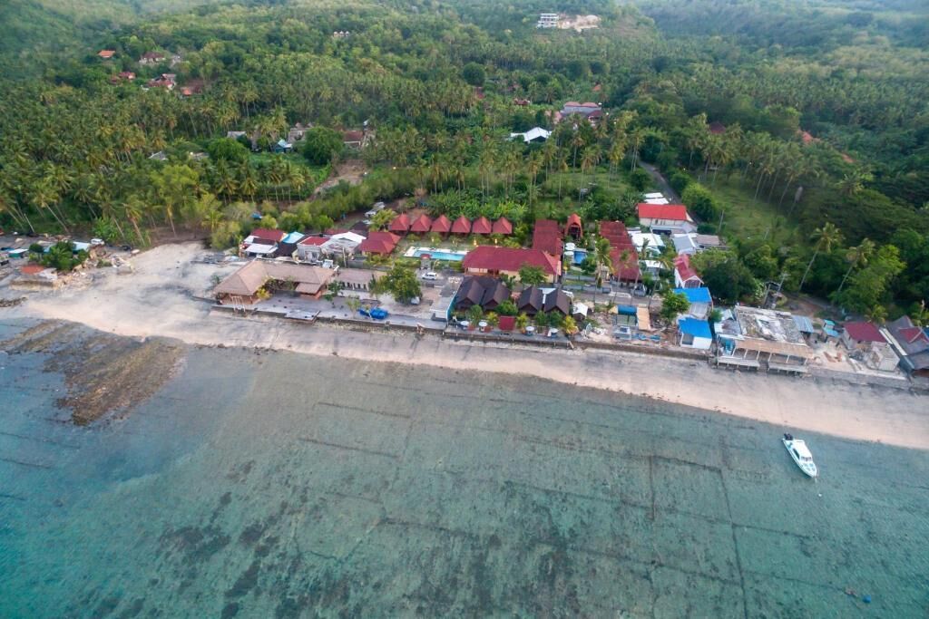 An aerial view of a coastal resort with multiple buildings, a beach, and a boat.
