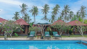 A pool area with lounge chairs and umbrellas, surrounded by palm trees and a wooden building with a red roof. - Rijet Villa Beach & Restaurant (Penida Island)