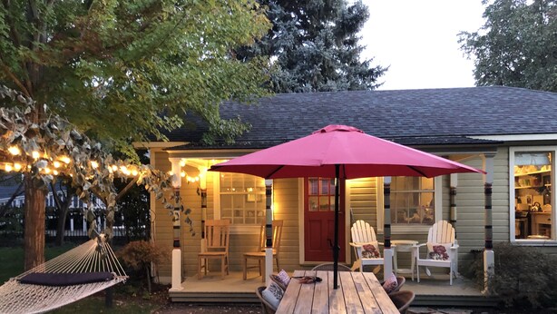 A cozy outdoor seating area with a wooden table and chairs, a red umbrella, and string lights. - Charming studio cottage on quiet street with beautiful landscaping and gardens. (Paonia)