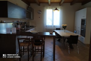 A modern kitchen with a central island, wooden chairs, a dining table, and a vase of flowers.