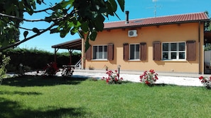 Uma casa com telhado de cerâmica, varanda coberta e jardim com flores vermelhas.