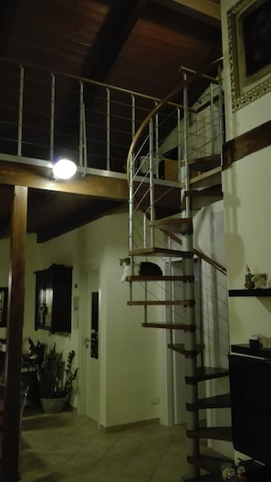 A spiral staircase with a metal railing, wooden steps, and a light fixture above.