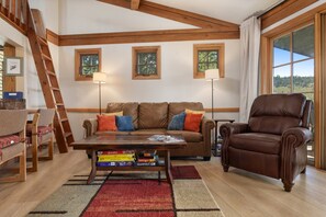 A cozy living room with a brown leather sofa, a wooden coffee table with board games, a brown leather armchair, and a wooden ladder. - 2 Bedrooms + Loft, Balcony w/ Great Views - Hot Tub - 30, Night Rentals + EZCancel (Steamboat Springs)