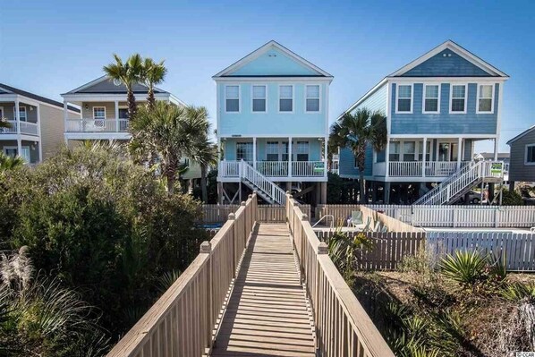 A wooden boardwalk leading to a row of beach houses with balconies and railings.