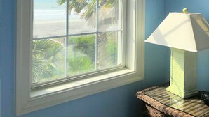 A room with a large window overlooking a beach, a lamp on a side table, and blue walls. - 5 Bedroom & 5 Bath Beachfront House w/ Private Pool, Hot Tub & Beach Boardwalk! (Surfside Beach)
