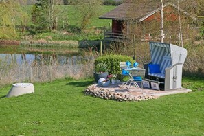 Un espace extérieur aménagé avec une table et des chaises, entouré d’une bordure en pierre, à proximité d’un étang et d’une structure en bois, dans un cadre rural.