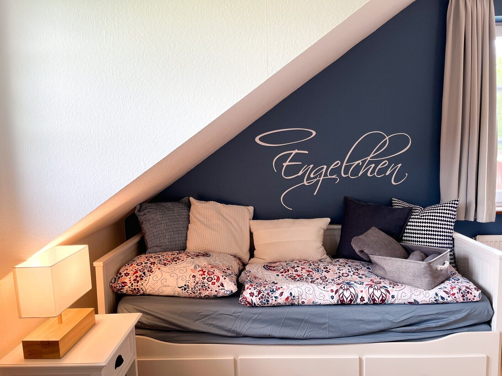 Um quarto aconchegante com teto inclinado, uma cama com roupa de cama estampada e um painel decorativo na parede.