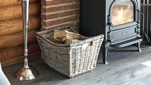 Ein gemütlicher Raum mit Backsteinwand, einem schwarzen Kaminofen, einem Korbwägelchen mit Holz und einem Kerzenleuchter mit Kerzen.