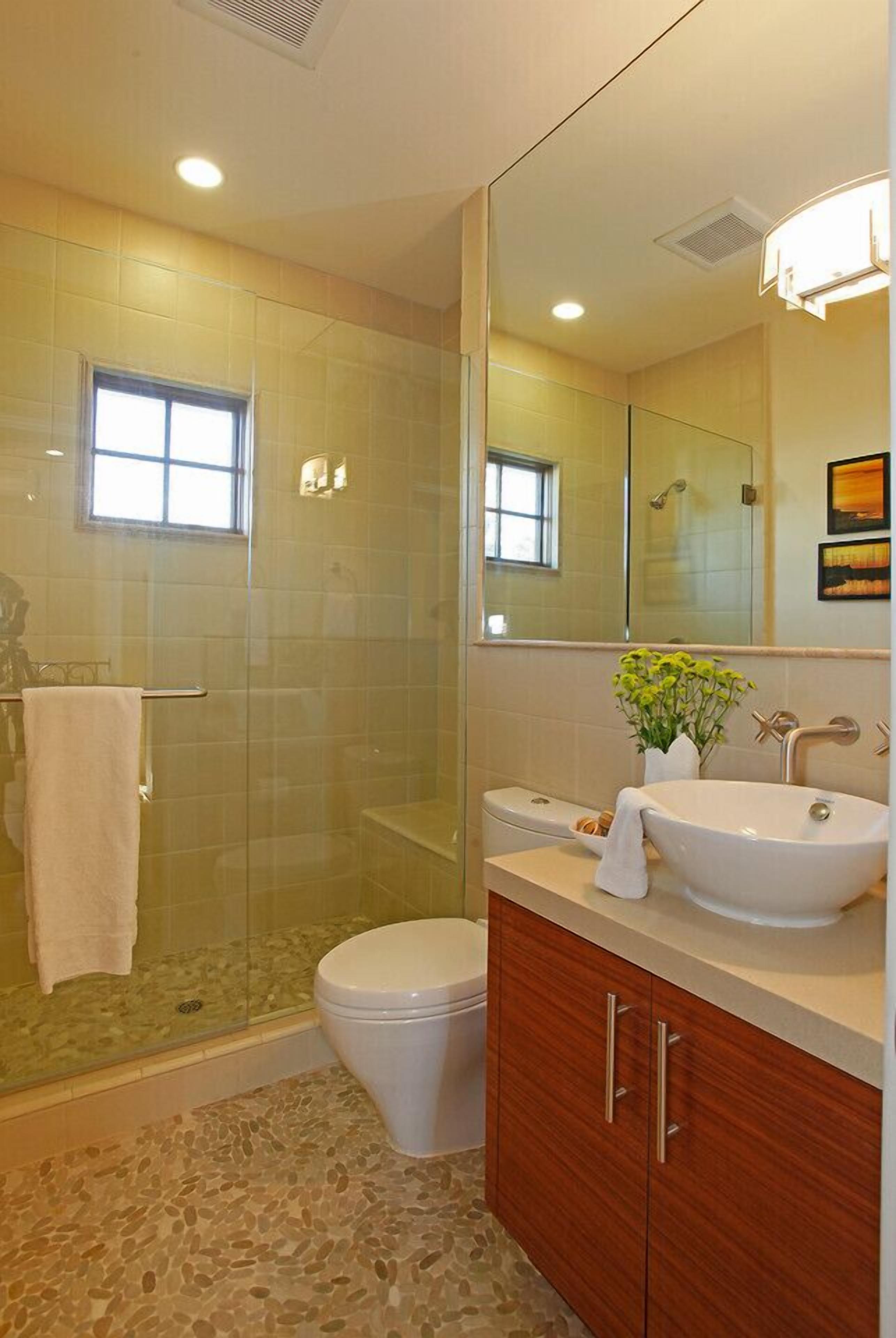 A bathroom with a glass-enclosed shower, a white toilet, a vanity with a sink, and a large mirror.