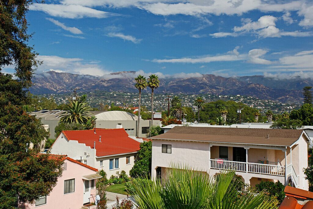 A residential area with houses, palm trees, and a mountainous backdrop.