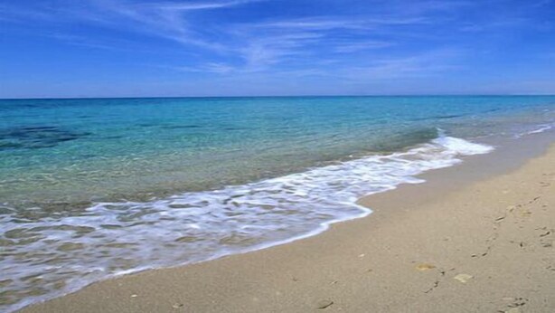 A beach with clear blue water and a sandy shore.