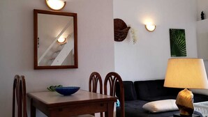Ein Essbereich mit Holztisch und Stühlen, einem Spiegel mit Wandleuchten, einem schwarzen Sofa und einem kleinen Beistelltisch mit Lampe.