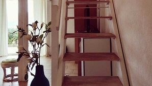 Eine Holztreppe mit einer Plattform im oberen Bereich, eine Vase mit Blumen im unteren Bereich und ein Stuhl im Hintergrund.