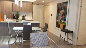 Una sala de estar moderna con una mesa de centro de vidrio, un sillón estampado y un comedor con una mesa y sillas blancas.