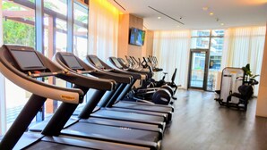 Un gimnasio con múltiples cintas de correr alineadas, un televisor montado en la pared y amplias ventanas que dejan entrar luz natural.