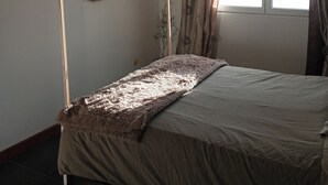 Un dormitorio con cama con dosel, un espejo redondo y una ventana con cortinas.