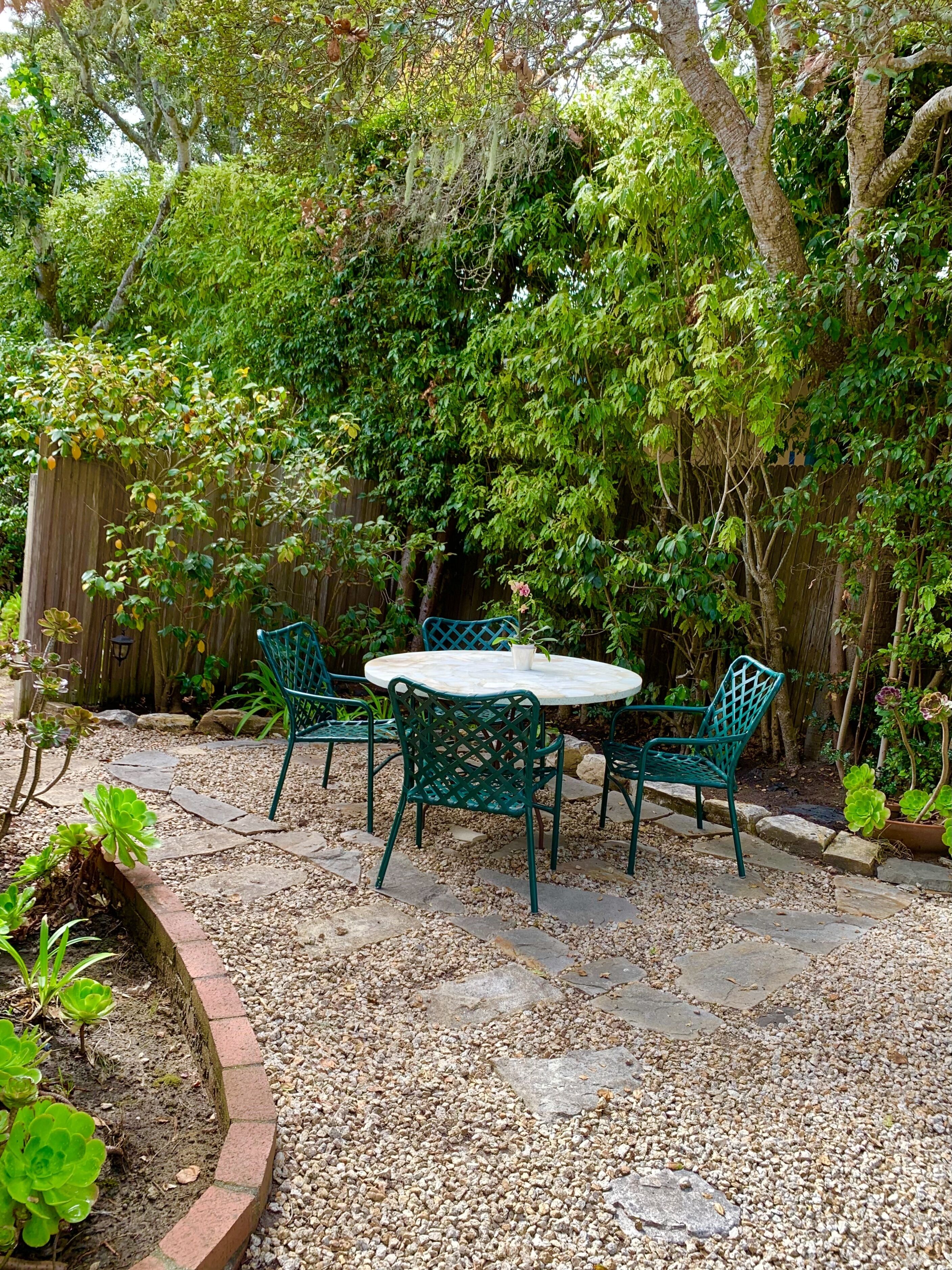 Une table ronde entourée de quatre chaises, dans un jardin.