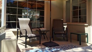 Un patio soleado con un paraguas grande color naranja, dos sillas, una mesita y un tapete estampado.