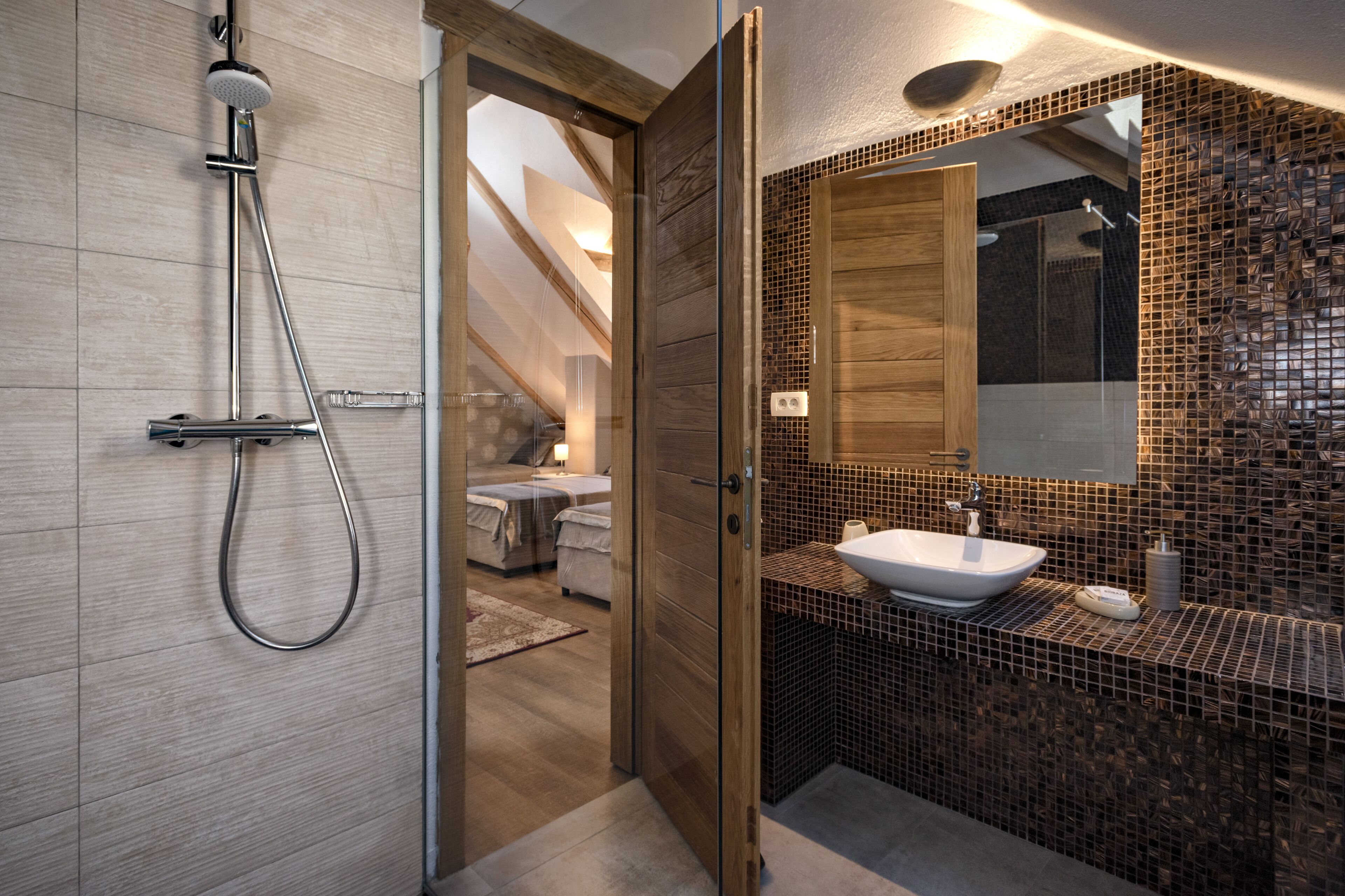 A modern bathroom with a glass shower enclosure, a wooden door, and a tiled vanity area.