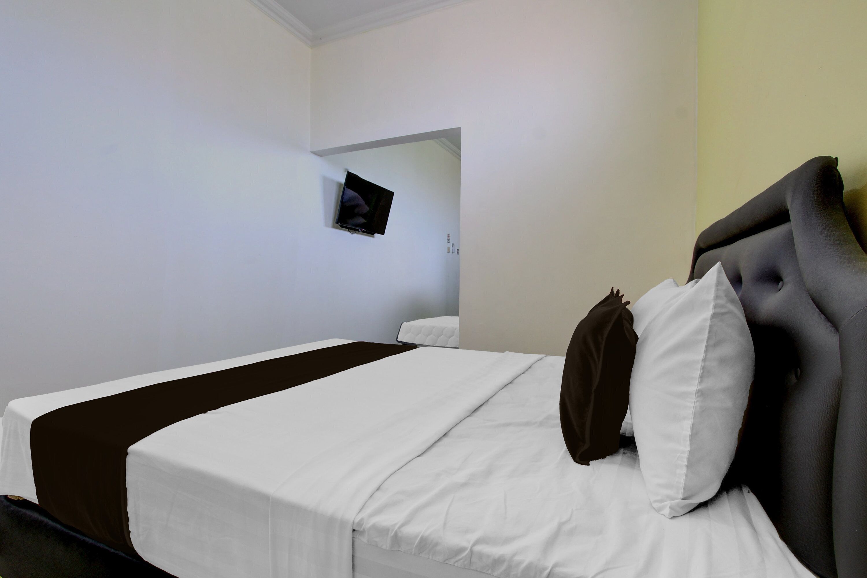 A hotel room with a bed, a television mounted on the wall, and a door leading to another room.